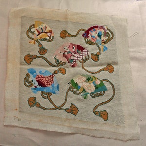 May include: A square needlepoint canvas featuring four distinct hand fans arranged on a light gray background. Each fan is connected by long, curved brown stems ending in tassels. The fans display varied patterns in yellow, red, pink, blue, and green.