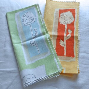 May include: Two rectangular fabric swatches with pinked edges. One swatch is light green with a central light blue rectangle and a black line-art flower. The other swatch is yellow with a central orange rectangle and a white line-art flower.