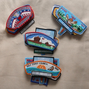 May include: A collection of Boy Scout patches, including a Heart of America Council BSA patch, a Kennesaw Mountain Council patch, a Gulf Coast Council patch, and an Egwa Tawa Dee patch. The patches are all embroidered with various colors and designs.