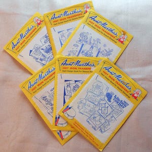 May include: Five yellow packages of Aunt Martha's Hot Iron Transfers. Each package features a different design and the text "Each Design Good For Several Stampings".