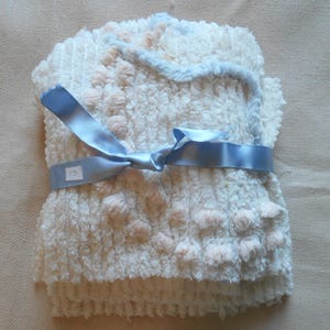 May include: A stack of white, textured washcloths with light pink accents and a light blue trim. The washcloths are tied with a light blue satin ribbon. A small tag with the number "13" is attached to the ribbon.