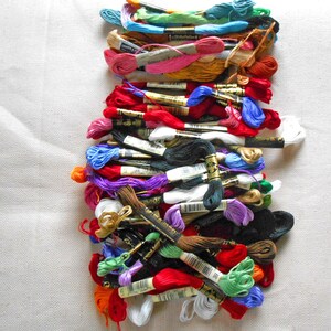 May include: A large collection of embroidery floss skeins in a wide variety of colors including red, blue, green, yellow, pink, purple, black, and white. Each skein features a paper label with a barcode and brand text wrapped around the thread.