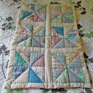 May include: A patchwork quilt with a cream background and a variety of colorful fabric squares. The quilt is made up of a grid of squares, each of which is made up of smaller squares. The quilt is edged with a cream border.