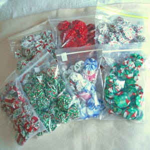 May include: Multiple clear plastic bags filled with assorted fabric yo-yos in various colors and patterns. The collection includes red, green, white, and blue fabric circles with festive holiday prints, floral designs, and gingham checks.