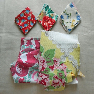 May include: A collection of fabric scraps with floral patterns. The scraps are in various shapes, including diamond and irregular forms. Colors include red, blue, yellow, green, and pink. The fabrics feature different floral designs, such as roses and small flower patterns.