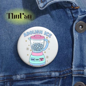 May include: A round, white button with a colorful illustration of a blender. The blender is pink and teal, with the words "ABOLISH ICE" in a blue arc above it. The button also has the words "PULSE", "BLEND", and "CRUSH ICE".
