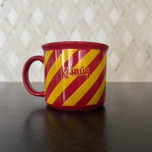 Puede incluir: Taza Kahlúa a rayas rojas y amarillas con asa roja. La taza presenta el logotipo de Kahlúa en color dorado. La taza de cerámica está diseñada para bebidas calientes.