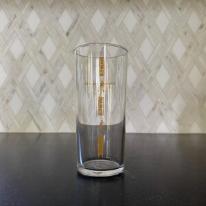 Puede incluir: Un vaso de vidrio transparente con una inscripci&oacute;n dorada que dice "Keep Walking" y "Johnnie Walker" en la parte delantera. El vaso est&aacute; sobre una superficie negra.