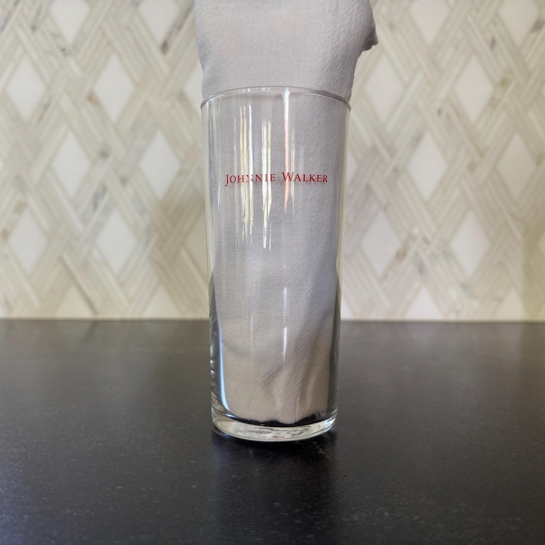 May include: A clear glass tumbler with the words "Johnnie Walker" printed in red on the side.