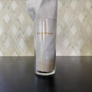 Puede incluir: Un vaso de vidrio transparente con las palabras "Johnnie Walker" impresas en dorado en el lateral.