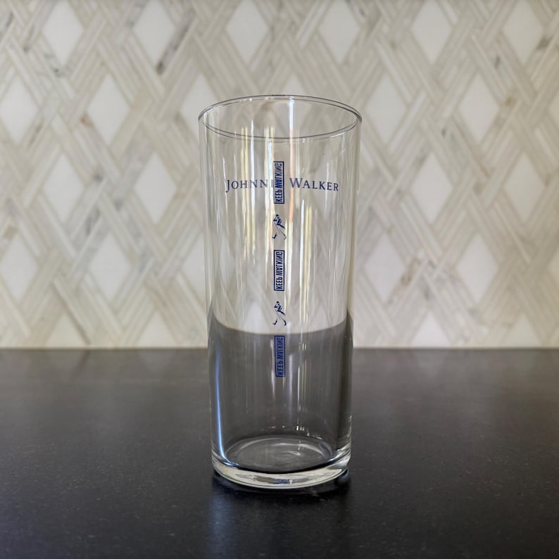 May include: A clear glass with the text "Johnnie Walker" printed on the side. The glass has markings for different measurements.