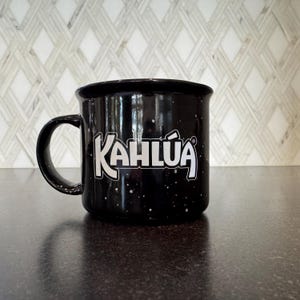 May include: Black ceramic mug with white speckles and the word "KAHLUA" in white lettering.