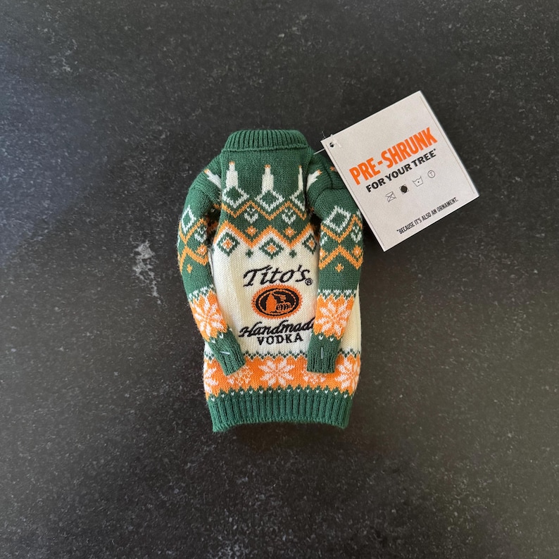Pu&ograve; includere: Un maglione per bottiglia lavorato a maglia verde, bianco e arancione con la scritta "Tito's Handmade Vodka". Il maglione ha un motivo festivo e un'etichetta che dice "Pre-Shrunk For Your Tree".