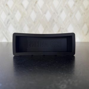 May include: A black rectangular rubber coaster with the embossed text "KEEP WALKING". The coaster has a curved design and is likely used to protect surfaces from drink condensation.