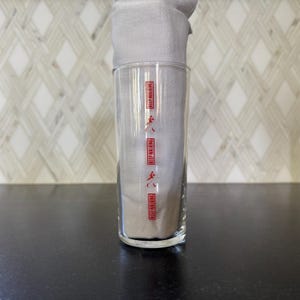 May include: A clear glass with the words "Keep Walking" repeated four times in red lettering on the side. The glass is sitting on a black surface.