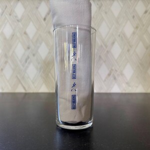 May include: A clear glass with the words "Keep Walking" printed on it in blue. The glass is empty and sitting on a black surface.