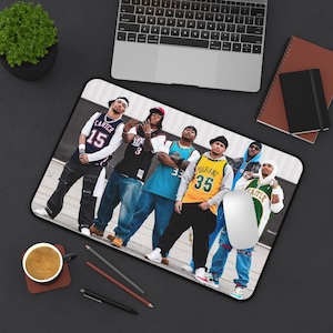 May include: Rectangular mousepad featuring a group of six people wearing jerseys and streetwear. The jerseys have numbers and names printed on them. The mousepad is on a black desk with a laptop, coffee cup, and other office supplies.