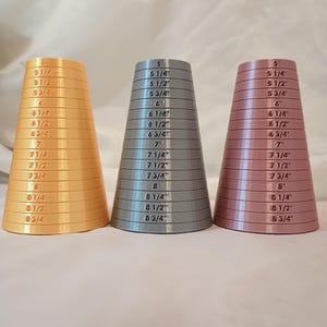 May include: Three graduated cone-shaped measuring tools in gold, gray, and pink. Each cone is marked with inch measurements from 5" to 8 3/4". The tools are designed with horizontal ridges and printed text.