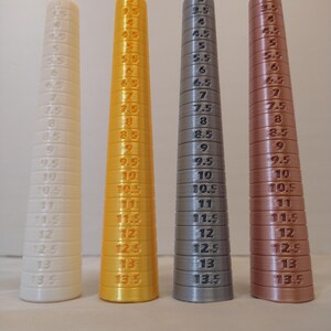 May include: Four ring sizers in white, gold, gray, and copper colors. Each sizer is a cone shape with ring sizes from 3 to 13.5 printed on the side. These tools are used to measure ring sizes.