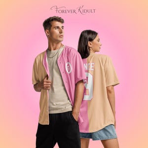 May include: Two people wearing baseball-style shirts with color-blocked designs. One shirt is pink and tan, the other tan and pink, with the word "NICE" and the number "9" on the back. The text "FOREVER KIDULT" is at the top.