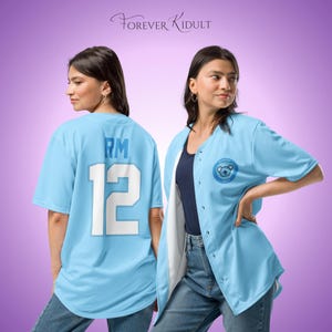 Peut inclure: Maillot de baseball bleu clair avec des détails blancs. Le dos affiche "RM" et le numéro "12". Un logo circulaire avec un ours est sur le devant. Le texte "FOREVER KIDULT" est en haut de l'image.