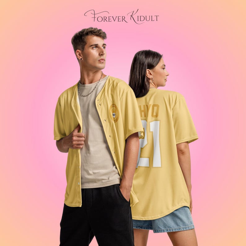 May include: Two people wearing yellow baseball jerseys with the text "HYO 21" on the back. The jersey on the left has a small emblem on the front. The text "FOREVER KIDULT" is at the top. The background is a gradient of pink and orange.