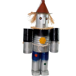 May include: A whimsical, handcrafted scarecrow figure made from recycled tin cans. The figure features a brown conical hat, straw hair, and a black and silver body. The arms are black cans, and the legs are blue and silver. A unique decorative item.