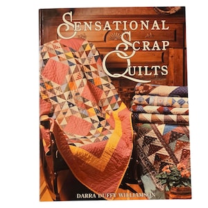 May include: A book titled "Sensational Scrap Quilts" by Darra Duffy Williamson. The cover features a colorful patchwork quilt draped over a wooden chair. The quilt is made of various fabrics in shades of red, pink, yellow, blue, and green. The book is a guide to creating beautiful quilts using scrap fabrics.