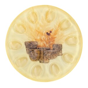 Peut inclure: Une assiette de service ronde, blanc cassé, avec un motif décoratif. L'assiette présente une image centrale de paniers tressés et de plantes séchées dans des tons bruns et beiges. Le bord extérieur comporte 12 cavités ovales. L'assiette est probablement en céramique ou en verre.