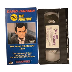 May include: A blue VHS tape box and tape for "The Fugitive" starring David Janssen. The box features a photo of Janssen and the text "The Final Judgement I & II". The tape is black with a white label.