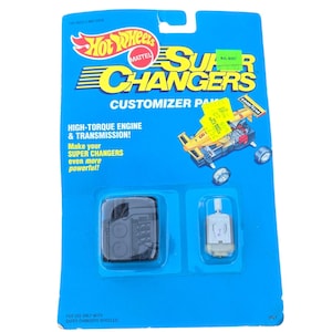 May include: A blue Hot Wheels Super Changers Customizer Pack. The package contains a black engine component and a silver motor. Text on the package reads "HIGH-TORQUE ENGINE & TRANSMISSION!" and "Make your SUPER CHANGERS even more powerful!"