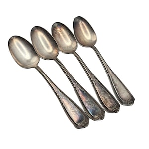 May include: A set of four silver-toned metal spoons with tarnished surfaces and ornate, engraved detailing on the handles. Each spoon features a tapered bowl and a decorative pattern near the base of the handle, showing signs of age and wear.