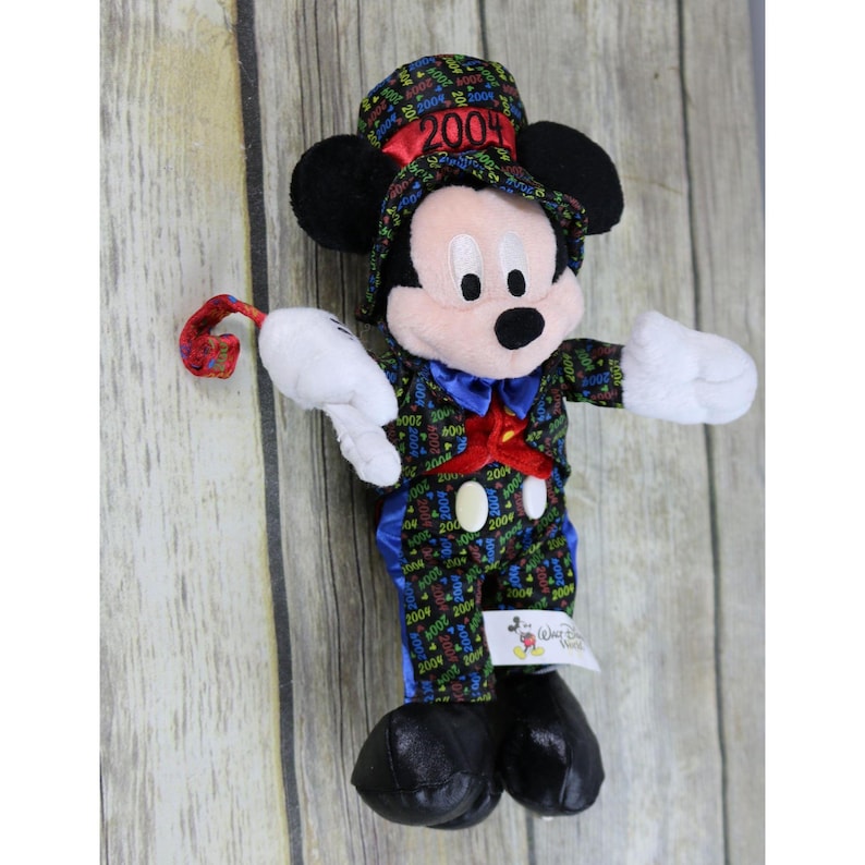 May include: A plush Mickey Mouse wearing a black and green suit with a red bow tie and a top hat that says "2004". The suit is covered in the number "2004" in various colors. Mickey Mouse is holding a red and green streamer in his right hand.