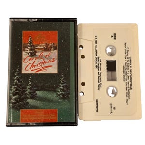 Puede incluir: Un casete vintage titulado "Carols of Christmas" con una portada verde y roja con una escena invernal. El casete es de color blanquecino con la lista de canciones impresa. El Coro del Tabernáculo Mormón aparece como intérprete.