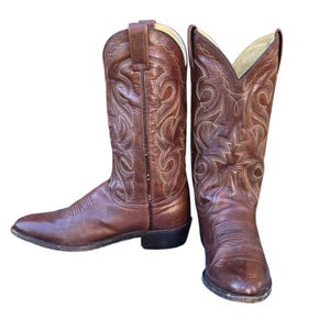 May include: A pair of brown leather cowboy boots. The boots have pointed toes, decorative stitching, and a pull-on design. The boots are approximately 12 inches tall.