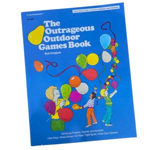 May include: A blue book titled "The Outrageous Outdoor Games Book" by Bob Gregson. The cover shows illustrations of balloons and children playing. The book includes 133 group projects, games, and activities.