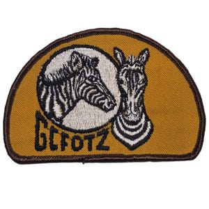 May include: A patch featuring two zebra heads in black and white, set against a tan background. The patch has a brown border and the text "GCFOTZ" in a stylized font.
