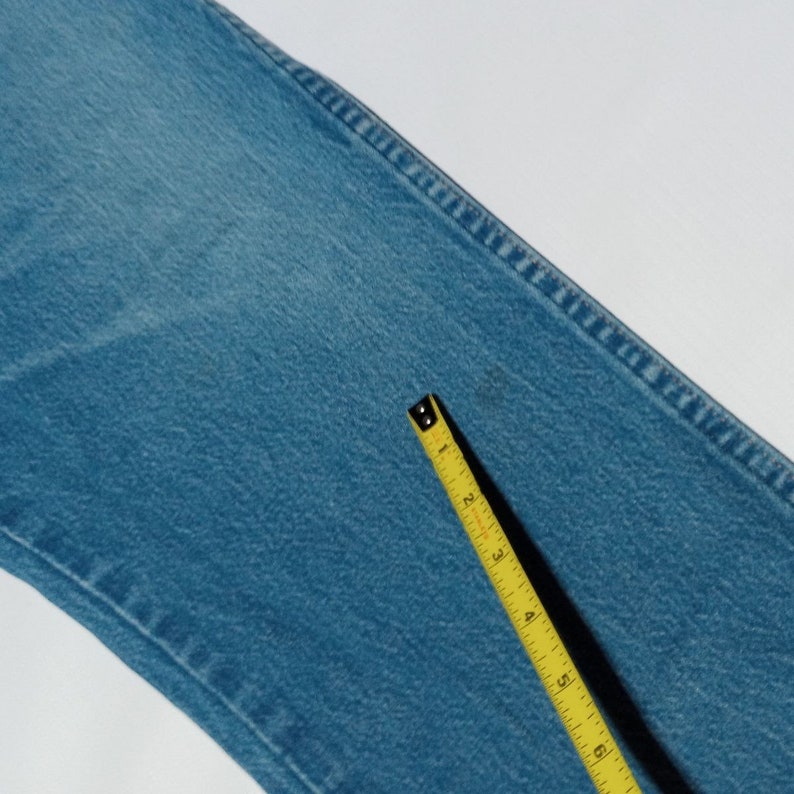 Puede incluir: Primer plano de una tela vaquera azul claro con una cinta m&eacute;trica amarilla. La cinta mide 15,24 cm.