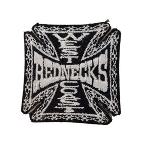 Puede incluir: Parche bordado en blanco y negro con un diseño de cruz y la palabra "REDNECKS" en el centro.
