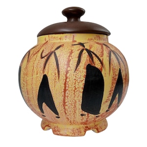 Puede incluir: Un tarro de cerámica redondo con tapa marrón. El tarro está decorado con diseños abstractos negros y amarillos.