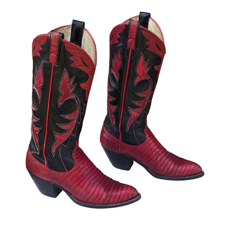 May include: A pair of red and black cowboy boots. The boots feature a textured red vamp and a black shaft with red decorative stitching. The heels are black, and the boots are set against a white background.