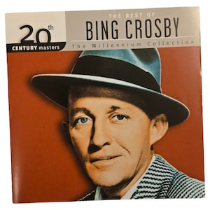 Peut inclure: Une pochette d'album de style vintage avec une photo en noir et blanc de Bing Crosby portant un fedora. Le titre de l'album est "The Best of Bing Crosby: The Millennium Collection" avec le texte "20th Century Masters" en dessous.
