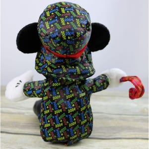 May include: A black plush Mickey Mouse wearing a black and red hat with a repeating pattern of "2004" in various colors. Mickey is holding a red and white curled party horn.