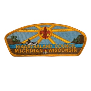 May include: A yellow and brown embroidered Boy Scout patch with a blue background. The patch features a sun with rays, a canoe, a campfire, and the text "Hiawatha Land Council Michigan Wisconsin".