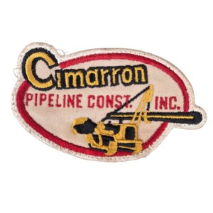 May include: Embroidered patch with the text "Cimarron PIPELINE CONST. INC." in black and red. The patch features a yellow and black construction vehicle design on a cream-colored background, framed by a red and white border.