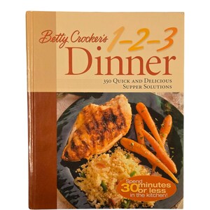 May include: A cookbook titled "Betty Crocker's 1-2-3 Dinner" with a photo of a plate of food. The food includes a grilled chicken breast, couscous, and carrots. The book cover states "350 Quick and Delicious Supper Solutions" and "Spend 30 minutes or less in the kitchen!"