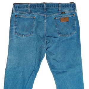 Puede incluir: Un par de pantalones vaqueros azules de mezclilla con un parche de cuero marr&oacute;n en el bolsillo trasero que dice "Wrangler".