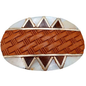 May include: An oval belt buckle featuring a central horizontal band of tan woven leather. The top and bottom sections consist of white iridescent shell inlays accented by dark brown triangular wood inlays, all separated by thin silver-toned metal lines.