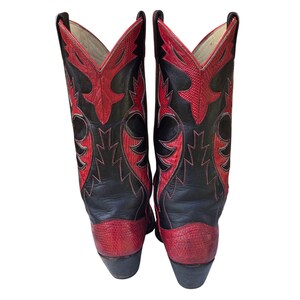 May include: A pair of black and red cowboy boots. The boots have a black leather upper with red detailing and stitching. The toe and heel are red, and the shaft features a decorative red pattern. The boots have a classic western design.
