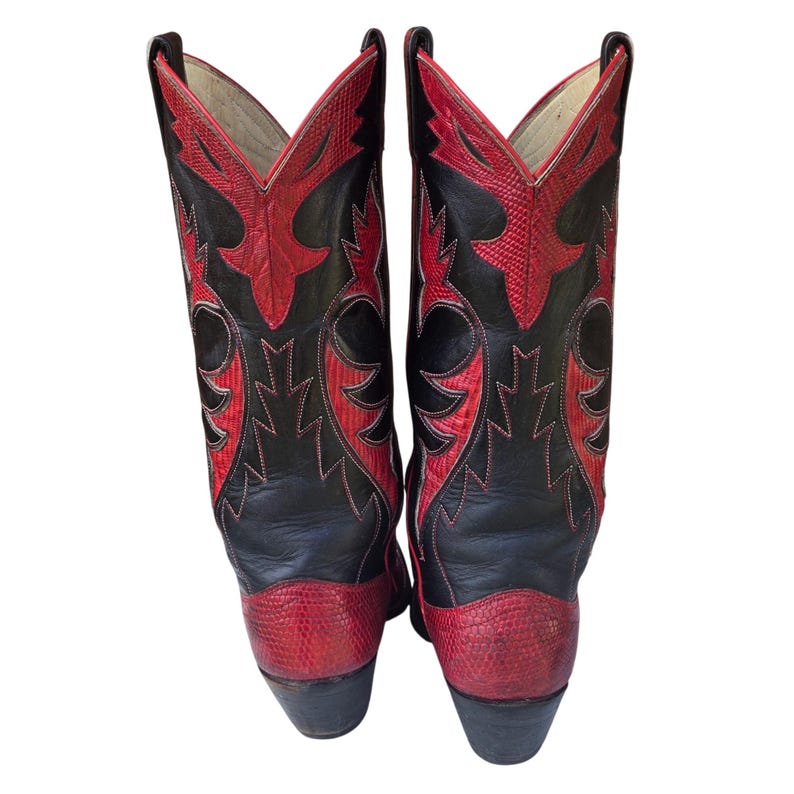 May include: A pair of black and red cowboy boots. The boots have a black leather upper with red detailing and stitching. The toe and heel are red, and the shaft features a decorative red pattern. The boots have a classic western design.